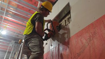 Construction worker cutting a wall with a power saw while standing on a ladder.