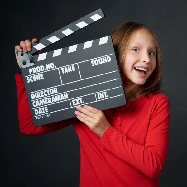 Young girl holding a movie clapperboard, smiling.