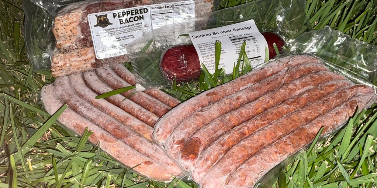 Assorted packaged meats including peppered bacon and smoked sausage on grass.