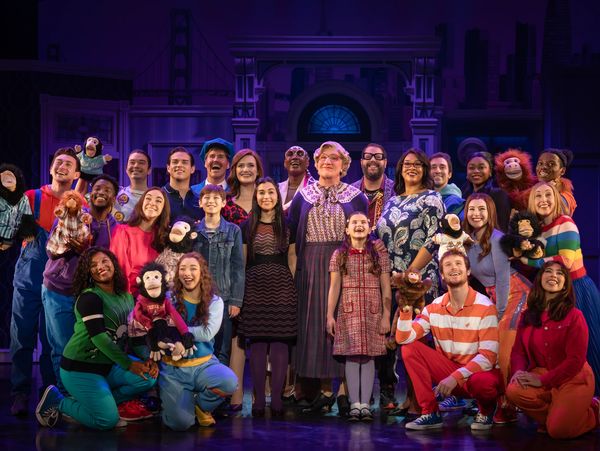 A diverse theater cast posing with puppets on stage.