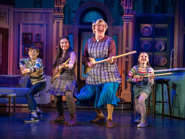 Four actors joyfully perform on stage with wooden props in a vibrant theatrical setting.