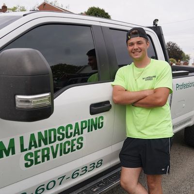 A young man in bright green shirt leans on a landscaping service truck.