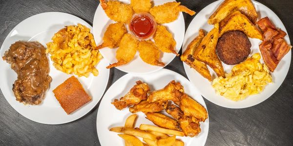 Four plates of comfort food including fried shrimp, chicken wings, mac and cheese, and breakfast items.