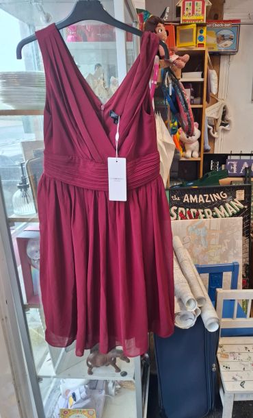 A sleeveless maroon dress hanging on a black hanger in a cluttered room.