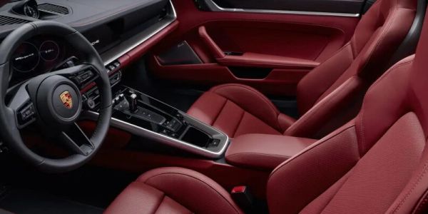 Luxury car interior with red leather seats and Porsche logo on steering wheel.