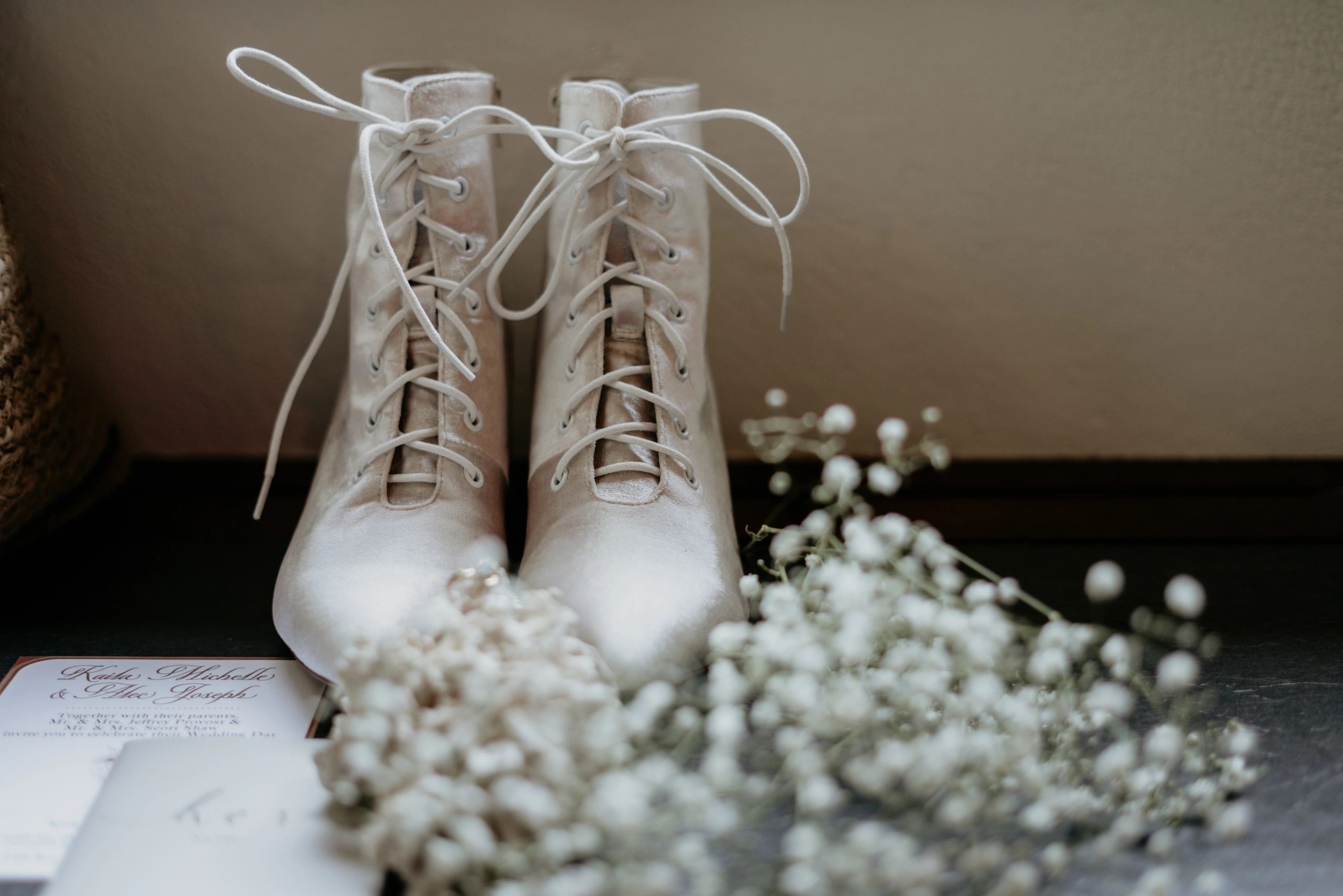 Elegant white lace-up boots with delicate flowers and a wedding invitation.