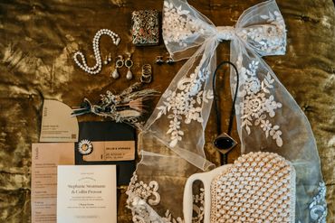 A vintage bridal accessory set with lace veil, pearl clutch, jewelry, and wedding invitations.