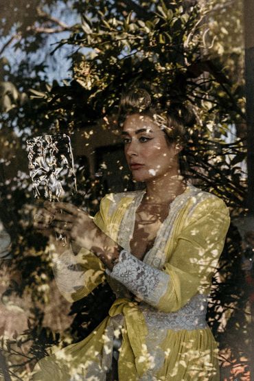 A woman in a yellow dress holding a vintage mirror among trees.