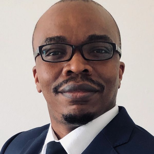 Man in glasses wearing a navy blue suit and tie, smiling slightly.