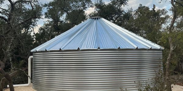 Large metal water tank with a conical roof surrounded by trees.