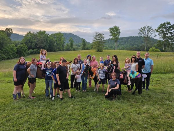 Group of people with ponies in a grassy field.