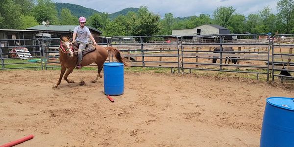 Person riding a horse around a barrel in an outdoor pen.
