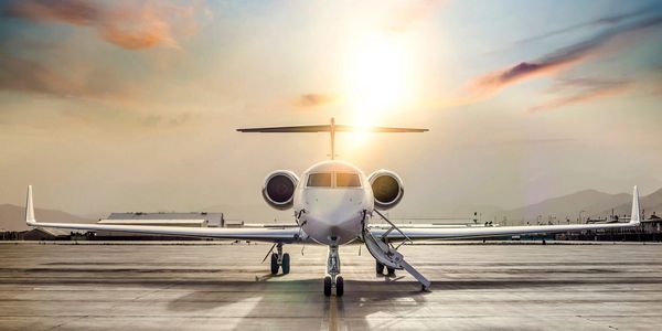 Private jet parked on runway with stairs down at sunset.