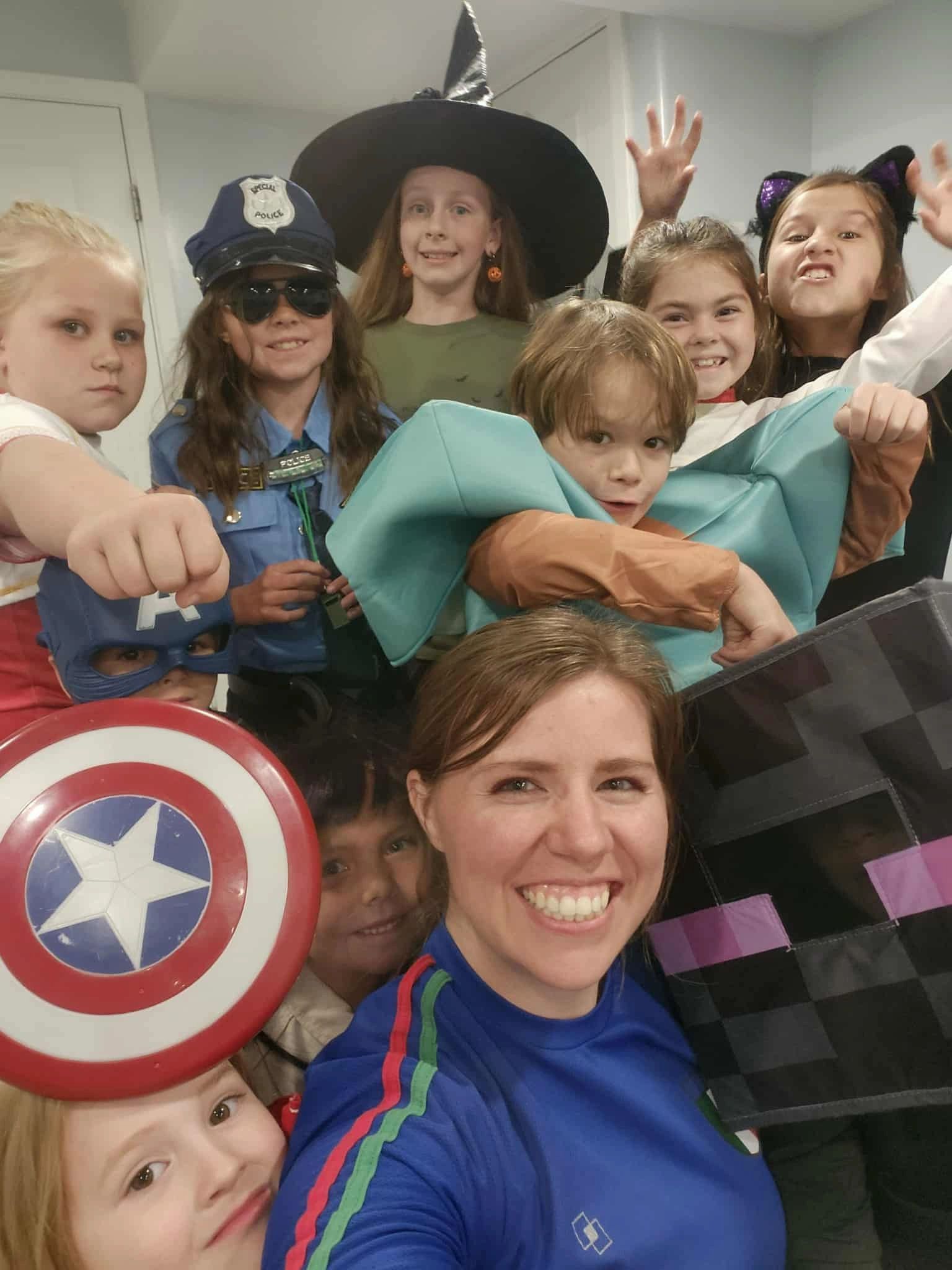 Group of children and an adult in various costumes smiling and posing for a selfie.
