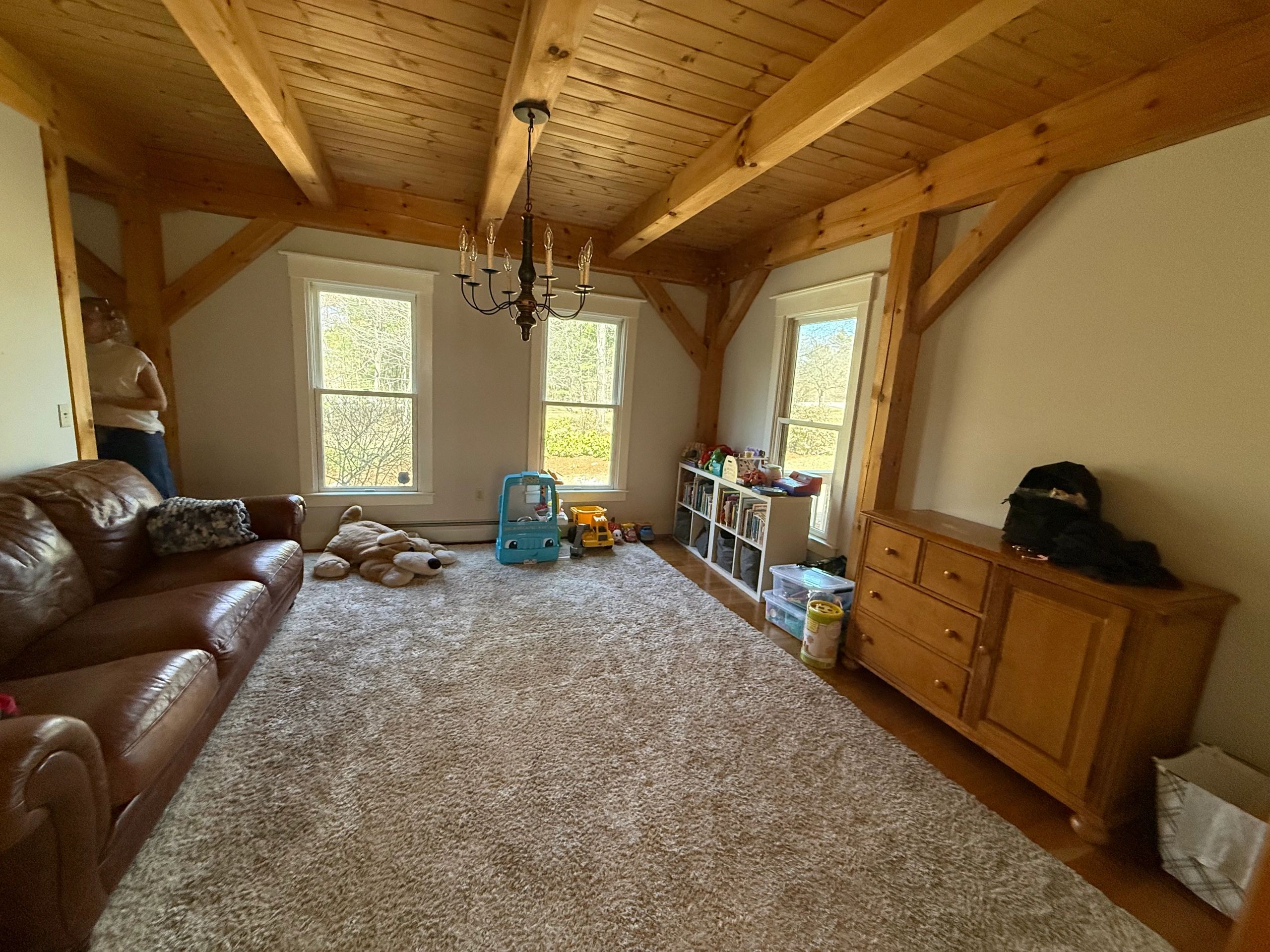 Cozy living room with wooden ceiling beams and children's toys by the windows.