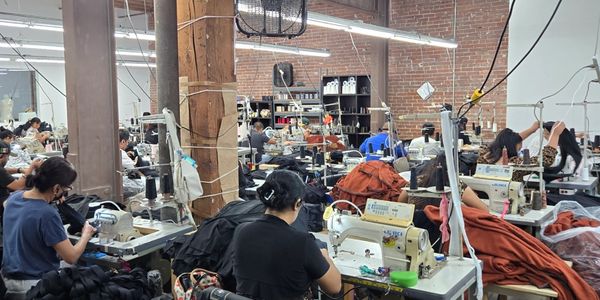 Workers sewing clothes in a busy garment factory with industrial machines.