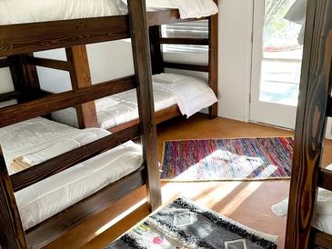 A cozy room with wooden bunk beds and colorful rugs on a sunny floor.