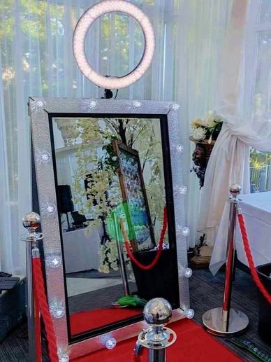 A large mirror with lights and a ring light behind red ropes on a red carpet.