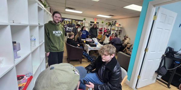 A group of young people socializing in a cozy, well-lit room with shelves and colorful decorations.