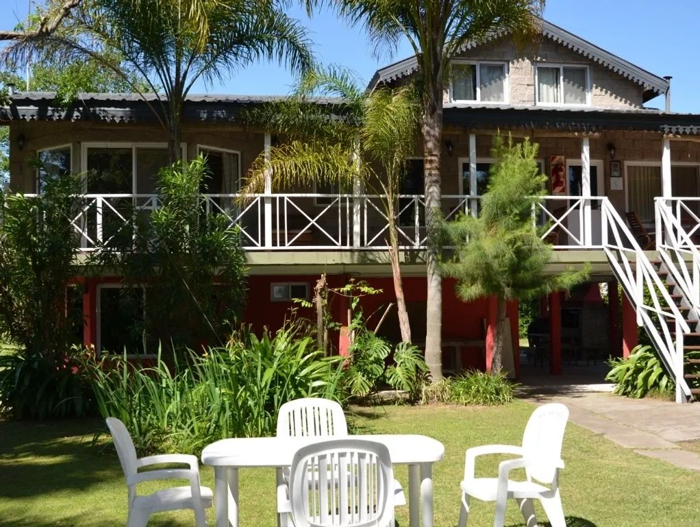Casa de dos pisos con terraza y jardín con muebles blancos.