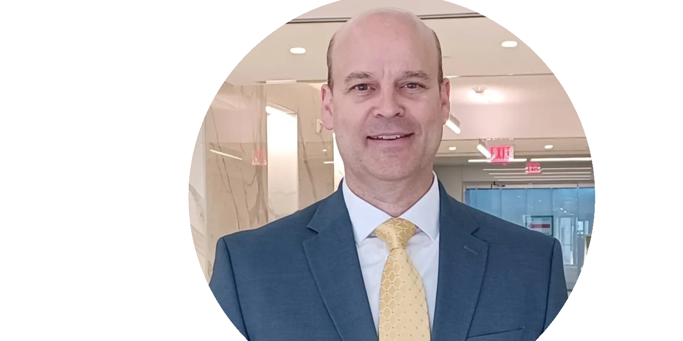 Smiling man in a suit and yellow tie in an office setting.