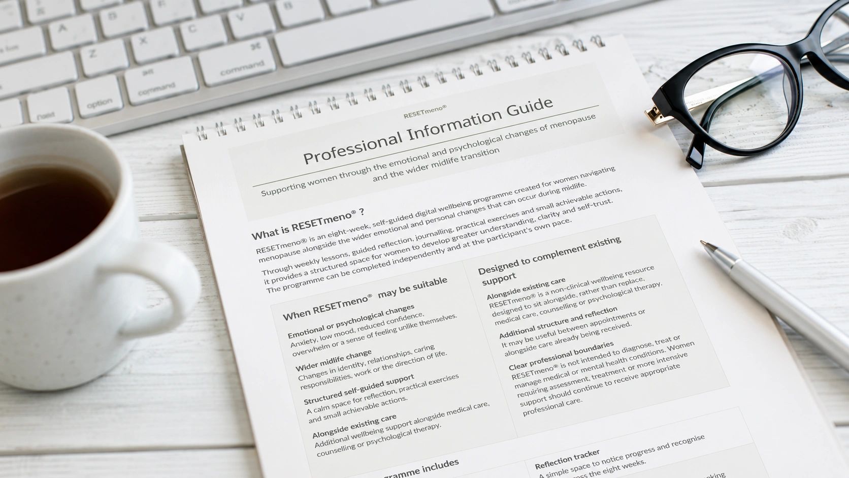 RESETmeno® Professional Information Guide on a desk beside a keyboard, glasses, pen and cup of tea.