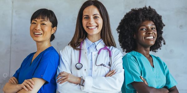 Three diverse female healthcare professionals smiling confidently with arms crossed.
