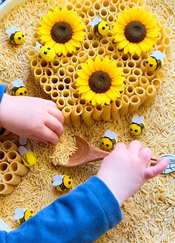 Child playing with bee-themed sensory activity using pasta and sunflowers.