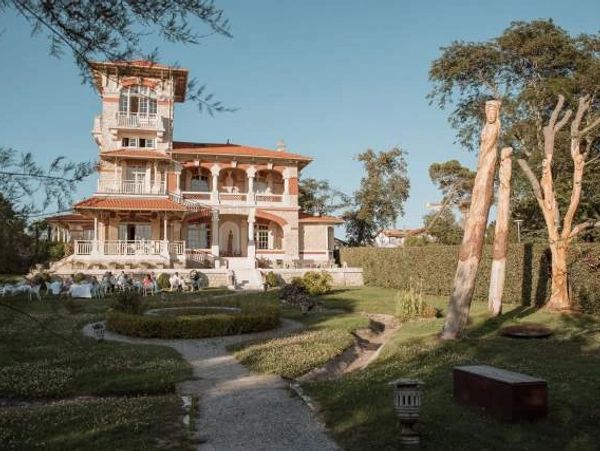 A large elegant mansion with a garden and sculptures under a clear blue sky.
