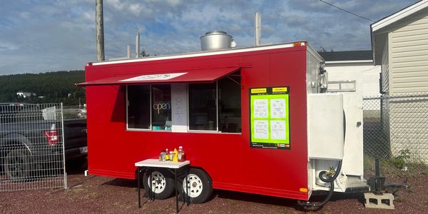 Red food truck with open service window and condiments on a small table outside.