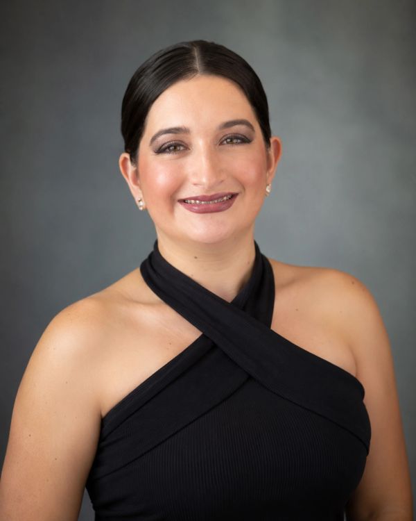 Woman smiling in a black halter top with a gray background.