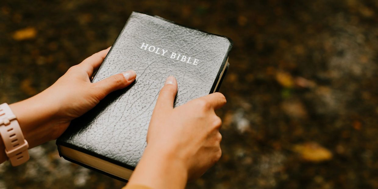 Person holding a black Holy Bible with both hands.