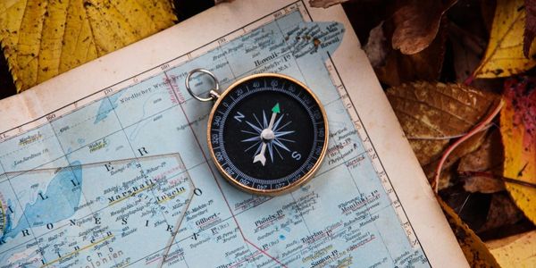 A compass resting on a vintage map surrounded by autumn leaves.