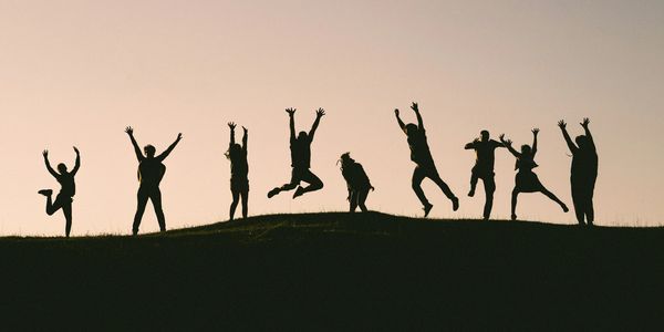 Silhouettes of people joyfully jumping on a hill at sunset.