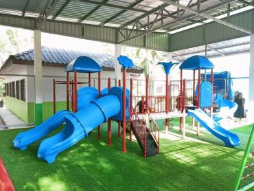 Bright blue playground slides under a sheltered area with artificial grass.