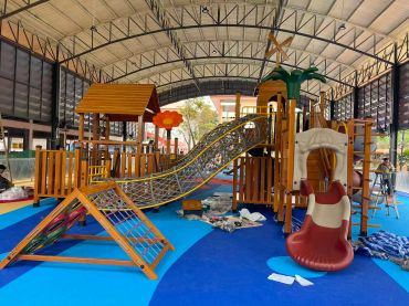 Colorful indoor playground with slides and climbing structures under a large roof.