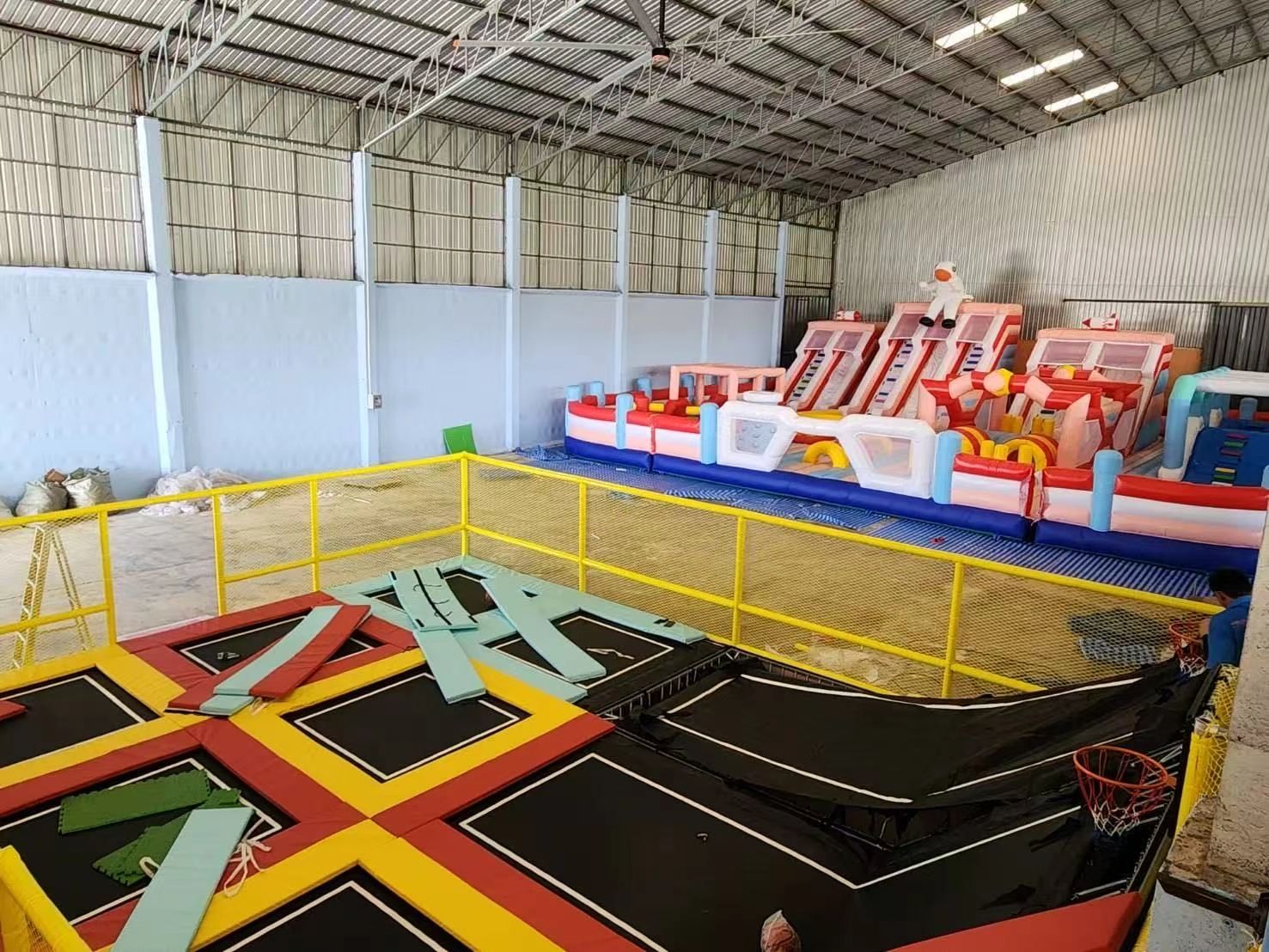 Indoor trampoline park with inflatable play structures and basketball hoops.