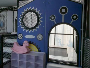 Indoor children's play area with a blue playhouse and pink rocking horse.