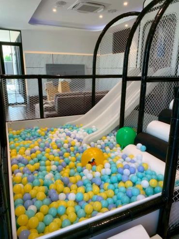 Indoor ball pit with colorful balls and a white slide in a modern living room.
