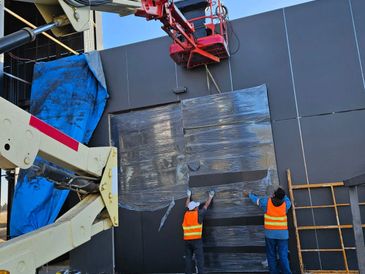 Workers installing large black panels on a building exterior using a lift.