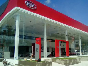 Modern Kia dealership with red and white branding under clear blue sky.