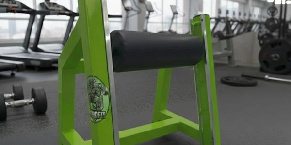 Green leg curl machine in a gym with weights in the background.