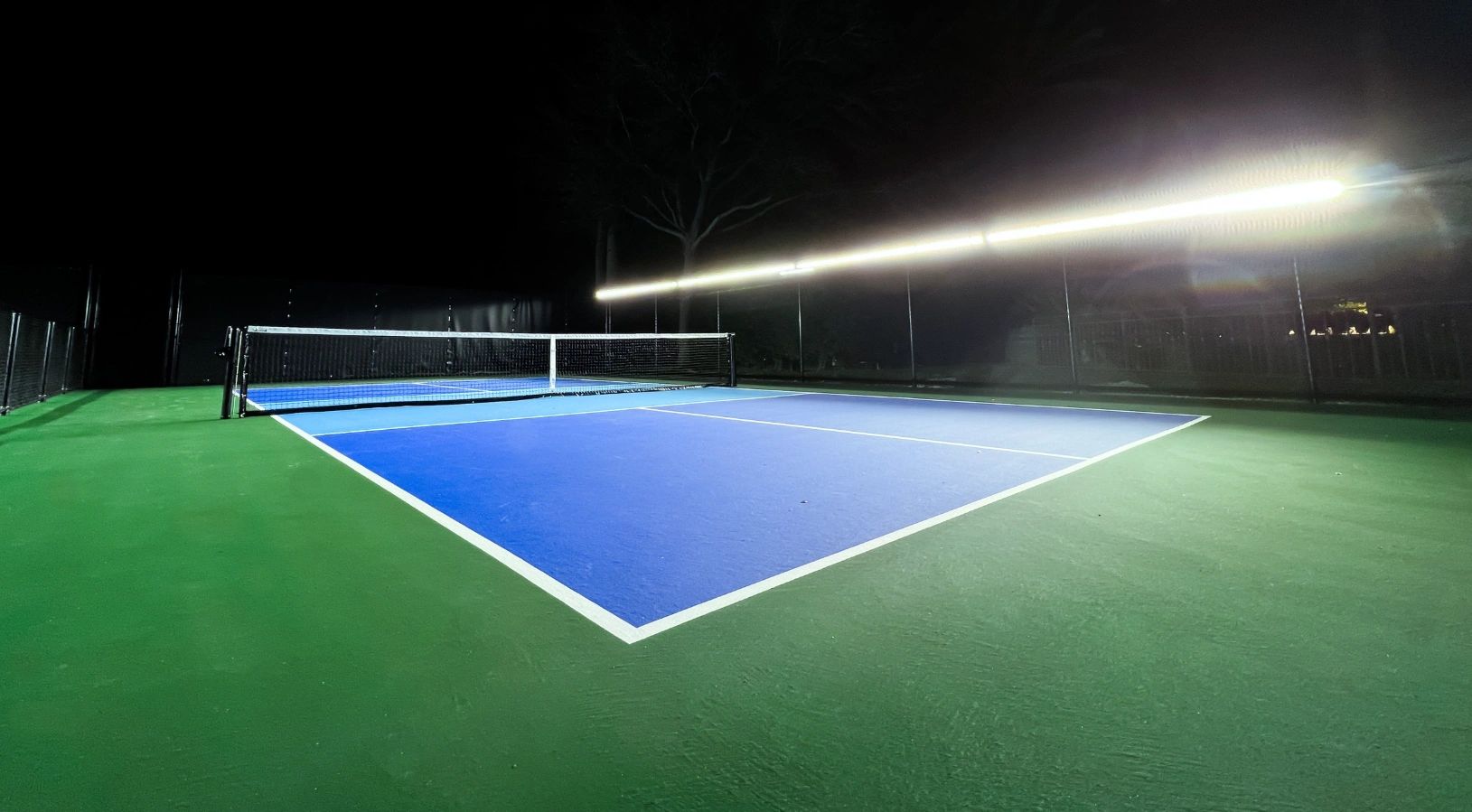 Empty tennis court illuminated at night with blue and green surface.
