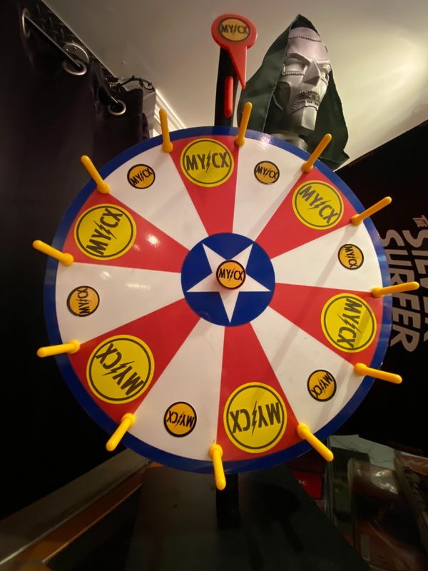 A colorful spinning prize wheel with yellow pegs and MY/CX logos.