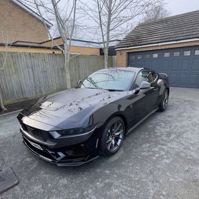 A sleek black sports car parked in a driveway beside a garage.