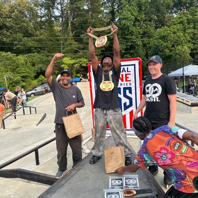 Three men celebrating a skateboarding event with trophies and smiles outdoors.