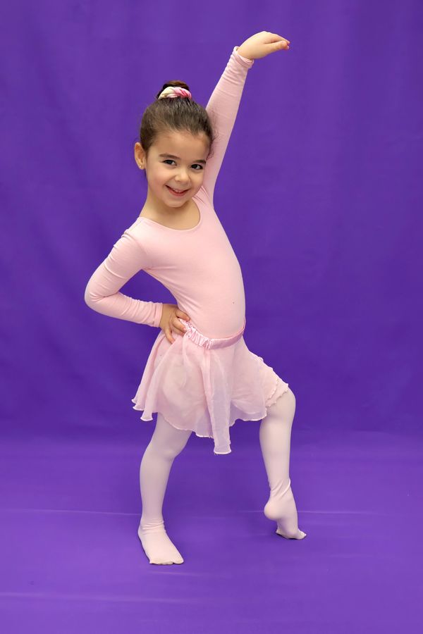 Young girl in pink ballet outfit posing against purple background.