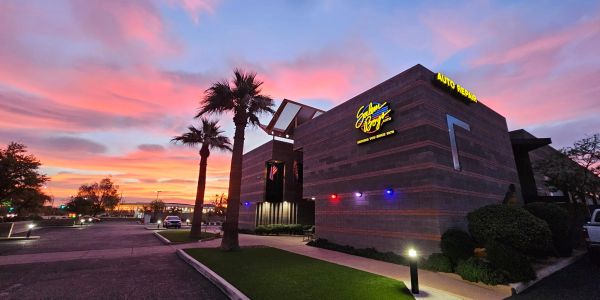 Modern building with neon signs at sunset under a colorful sky.