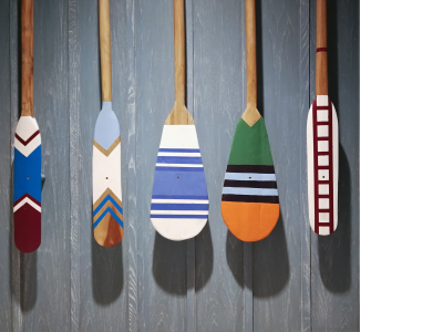 Five colorful wooden oars hanging against a gray wooden wall.