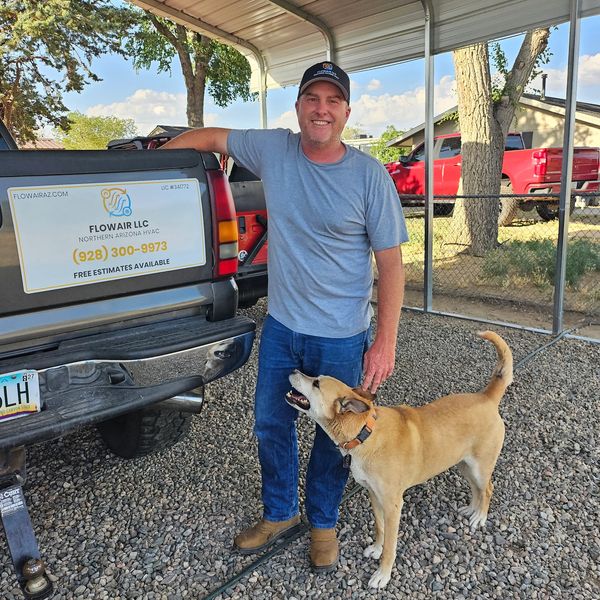 Man in casual wear with a dog standing beside a truck with a business sign.